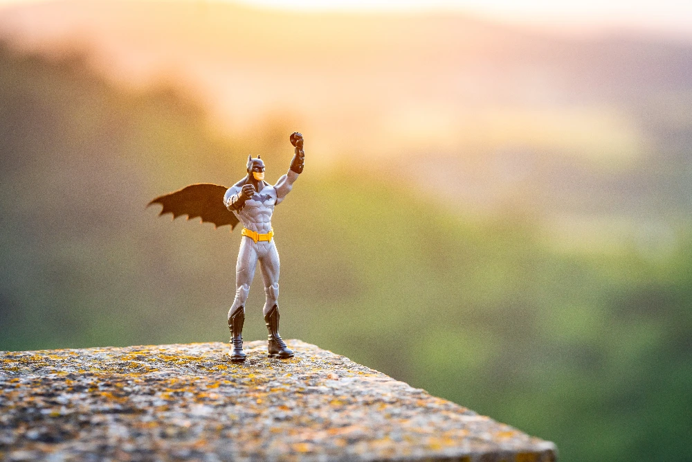 Mała figurka Batmana stojąca na murku na tle zachodzącego słońca – symbol lidera, który pomaga firmie rosnąć i porządkować chaos.